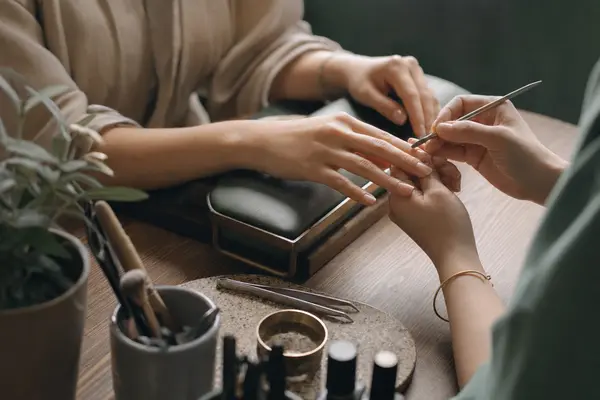 Nageldesignerin feilt einem Gast am Manikürtisch die Nägel