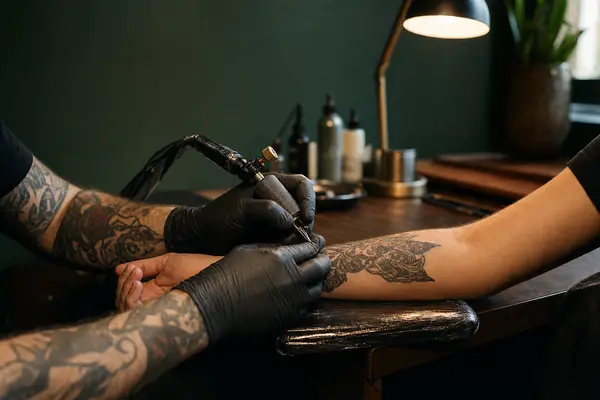 Tätowierer sticht ein Tattoo auf den Unterarm eines Gastes